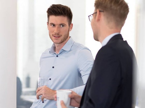 Zwei Kollegen stehen mit Kaffeetassen sich gegenüber