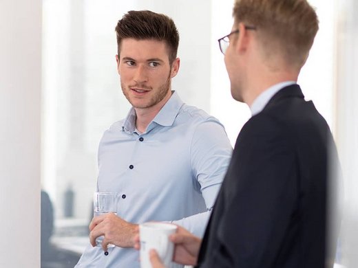 Zwei Kollegen stehen mit Kaffeetassen sich gegenüber