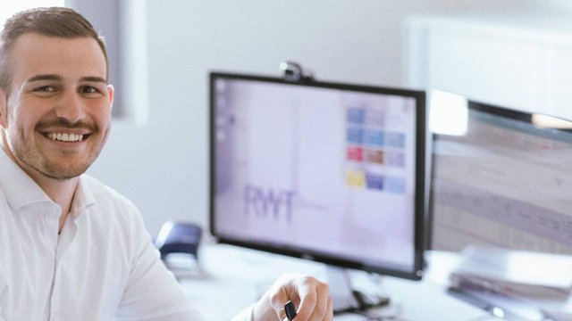 Eine Person sitzt auf Schreibtisch dreht sich aber weg zur Kamera und lächelt