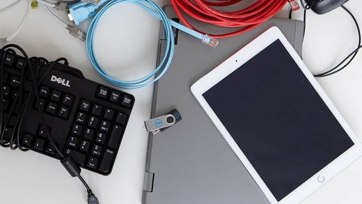 Ein Laptop, eine Tastatur sowie ein USB-Stick liegen auf einem Tisch und werden für ein IT Audit gebraucht