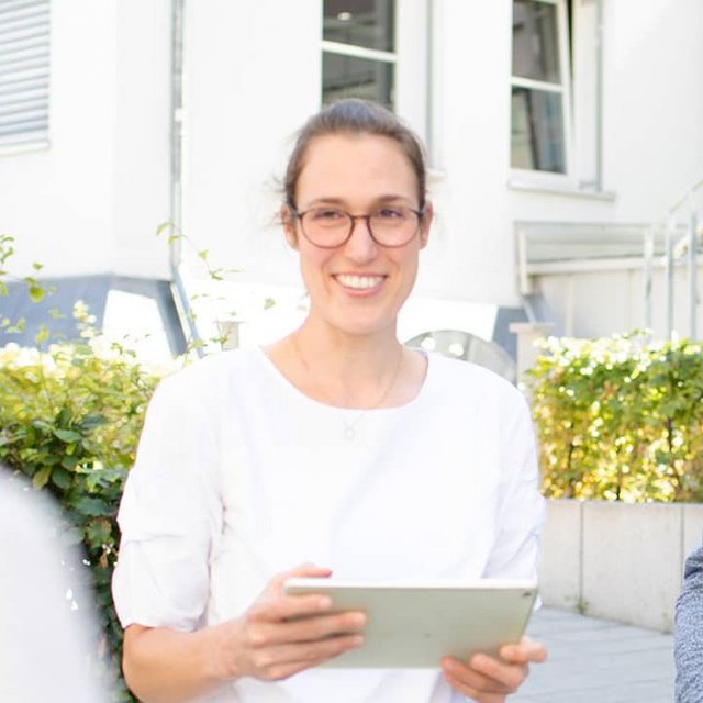 Drei Personen stehen draußen vor einer Steinmauer, die Frau hält ein Tablet in der Hand